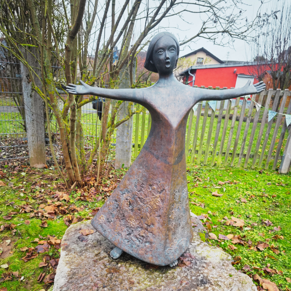 Das Bild zeigt eine Bronzeskulptur von einem singenden Mädchen im Skulpturenpark Elz